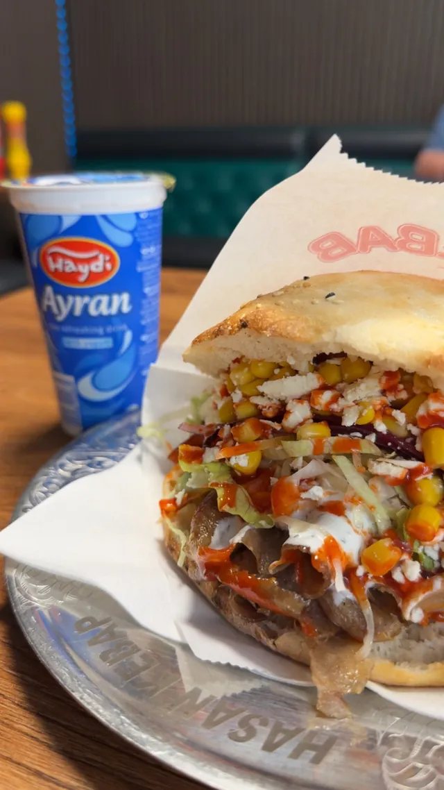 Döner im Fladenbrot mit Mais, Schafskäse, Salat und Soßen, daneben ein Ayran