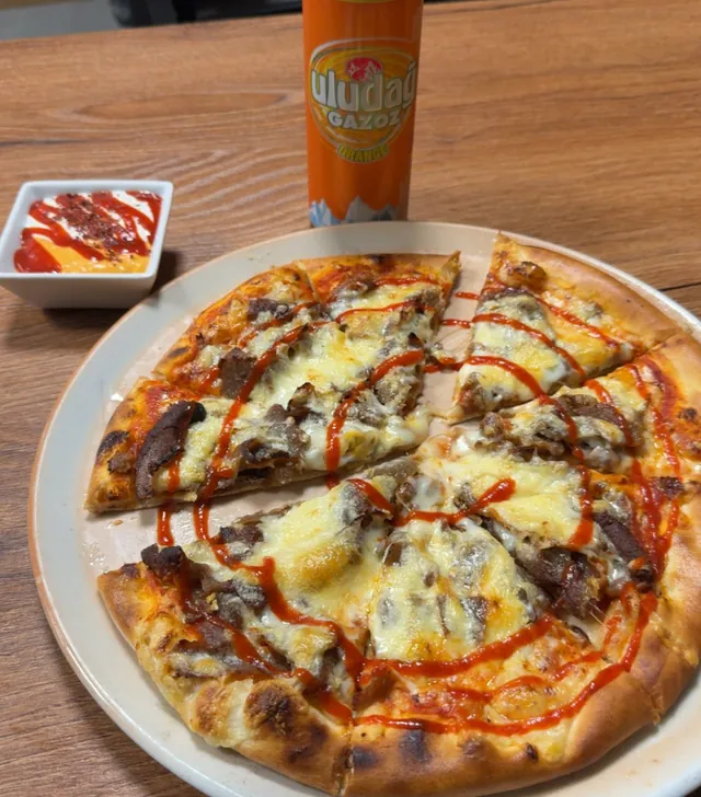 Döner Pizza mit Käse und scharfer Soße, daneben eine Dose Orangenlimo